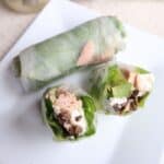 two halves of a spring roll facing up, showing tuna inside, a whole spring roll on the plate in the background