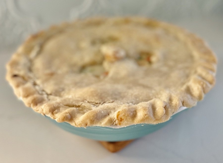 baked pie with a focus on the golden brown edge of the top crust, in a teal pie pan on a marble counter