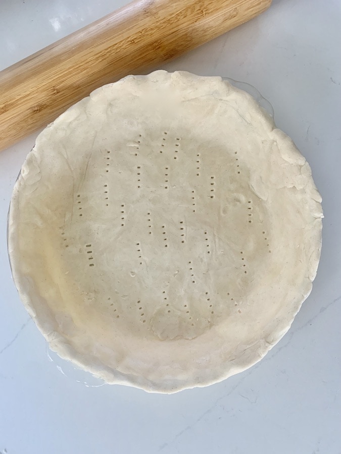 pie crust dough in a glass pan, uncooked, with fork holes along the bottom, birds eye view