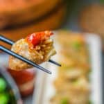 chopsticks holding a rice dumpling, with more food blurry in the background