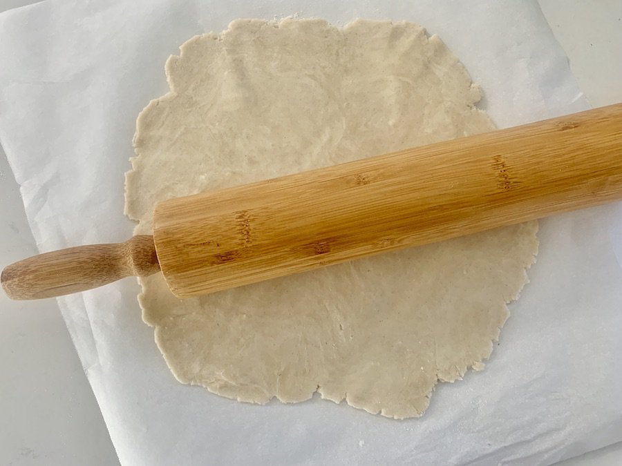 pie crust rolled out on parchment paper, bamboo rolling pin on top