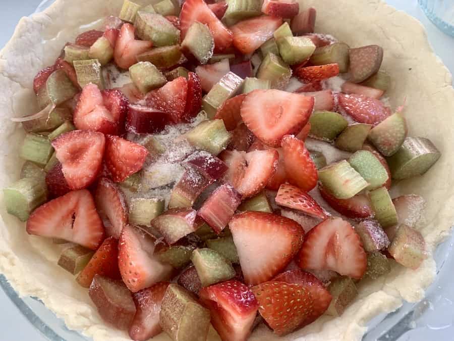 sliced red strawberries and green and red/pink rhubarb filling a pie shell