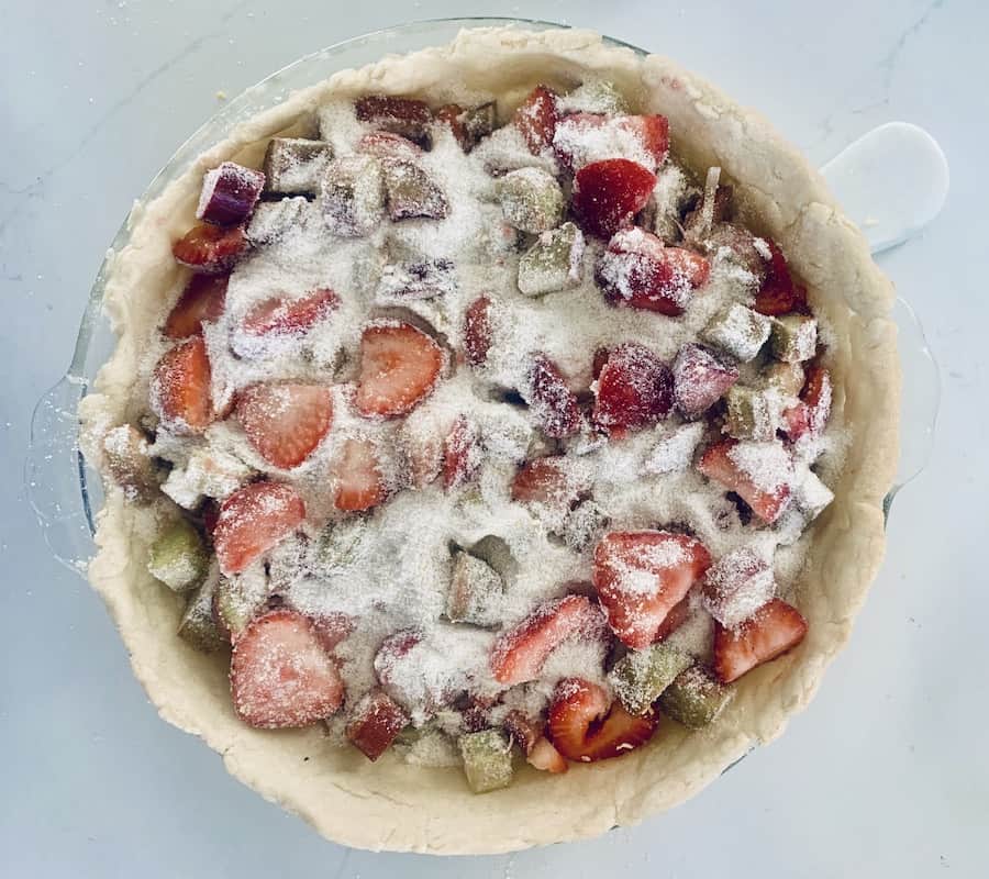 sliced red strawberries and green and red/pink rhubarb covered with flour in a pie shell, top view