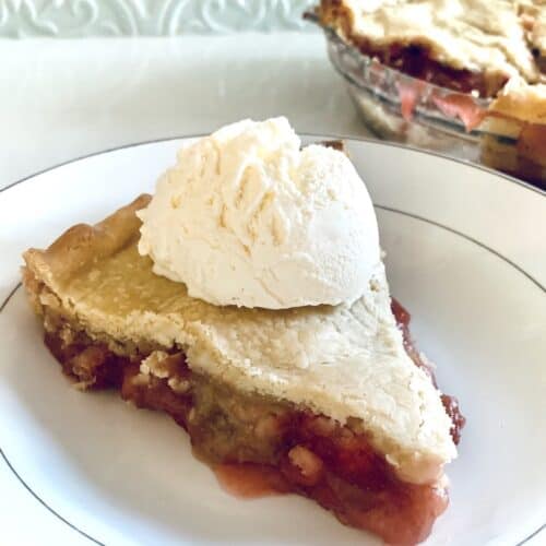 slice of gluten-free strawberry rhubarb pie with ice cream on top... part of the rest of the pie in the background