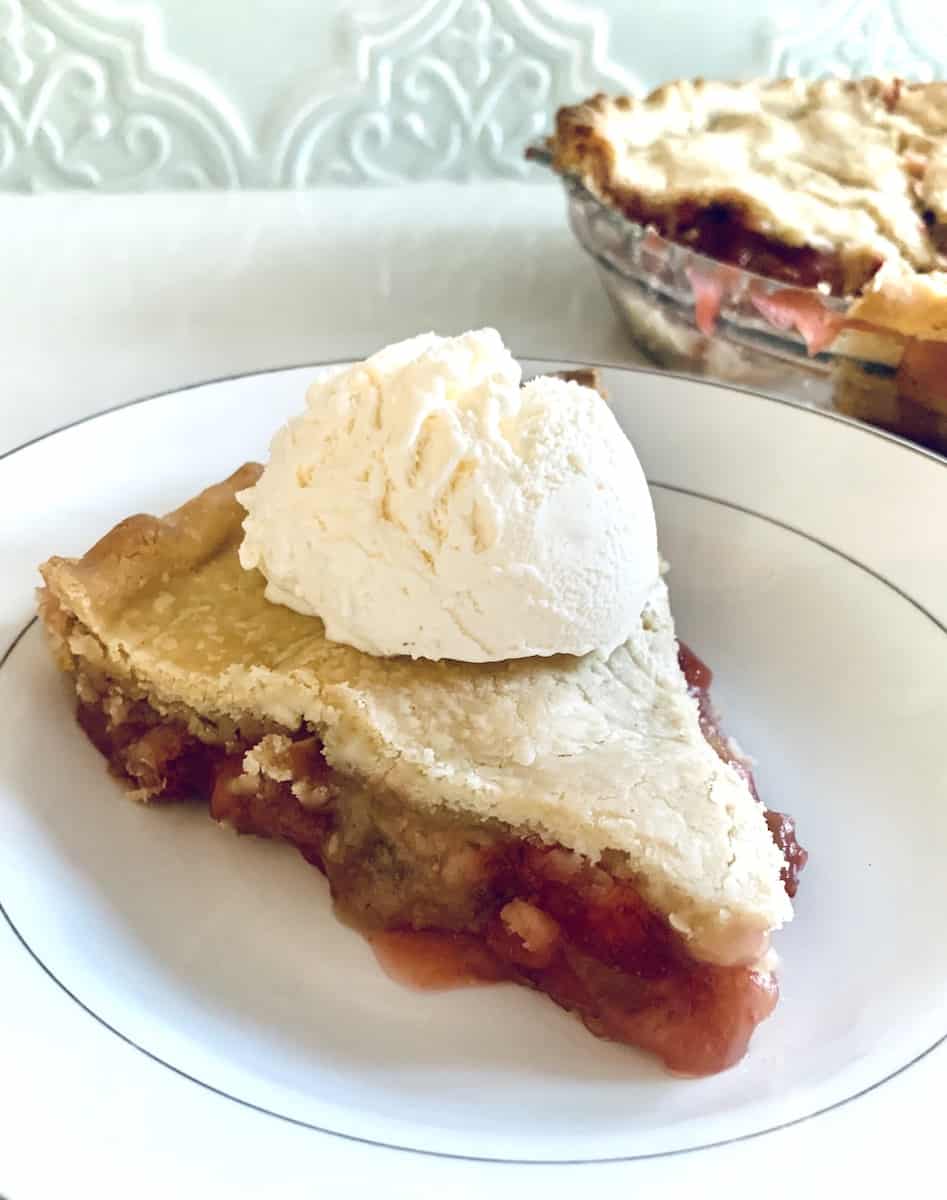 slice of gluten-free strawberry rhubarb pie with ice cream on top... part of the rest of the pie in the background