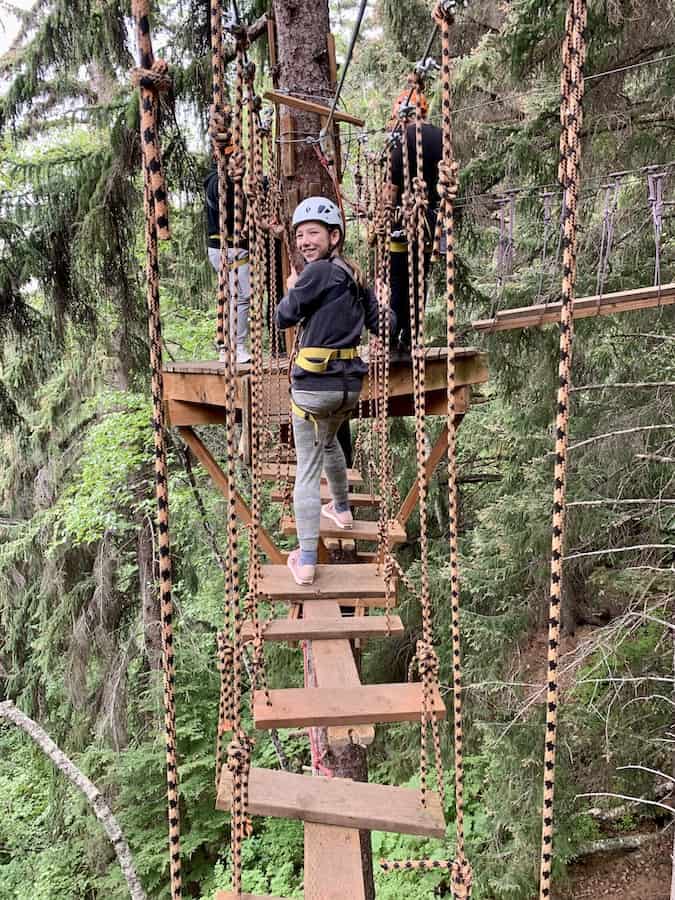 Miss E on a ropes course bridge, looking back and smiling