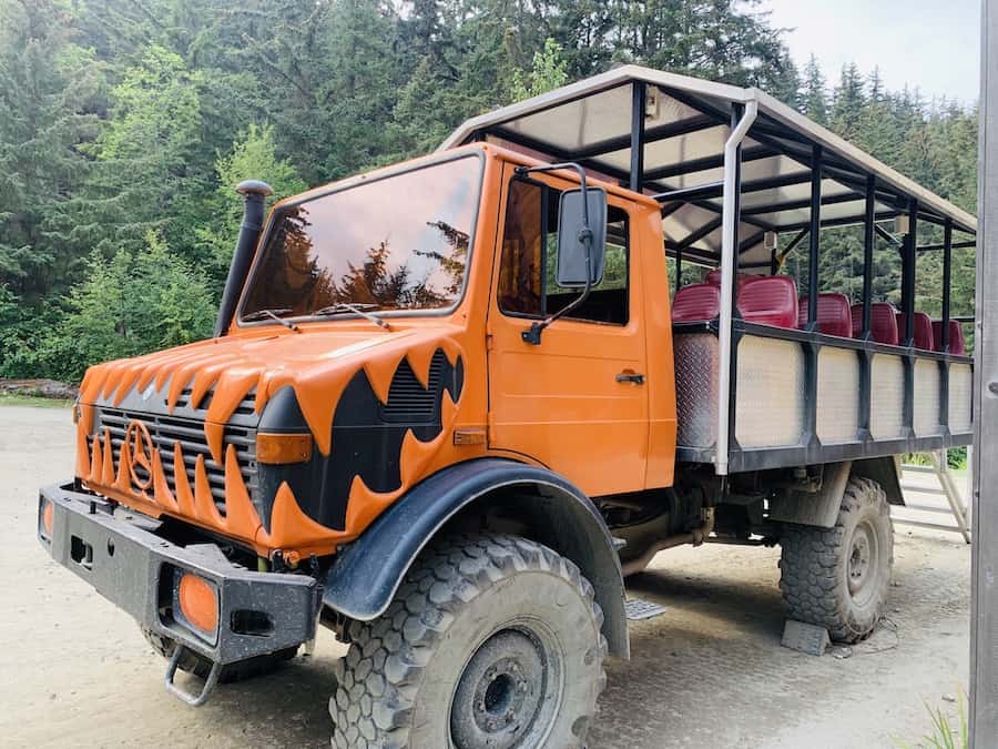 Unimog with big tires, an orange cab with a scary, black, zig-zag mouth painted on the grill, back is a covered area with red seats for about 20+ passengers