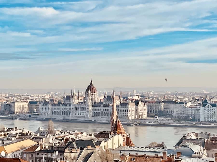city view of Budapest along both sides of the Danube... hot air balloon in the air, domed parliament building