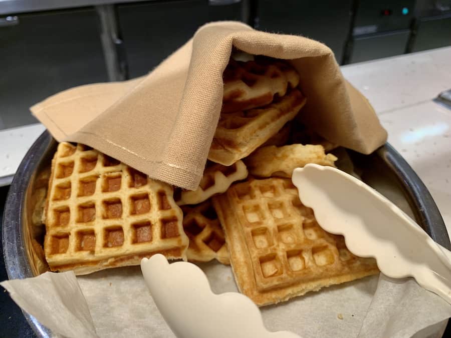 gluten-free waffles covered with a paper towel, tongs on the side