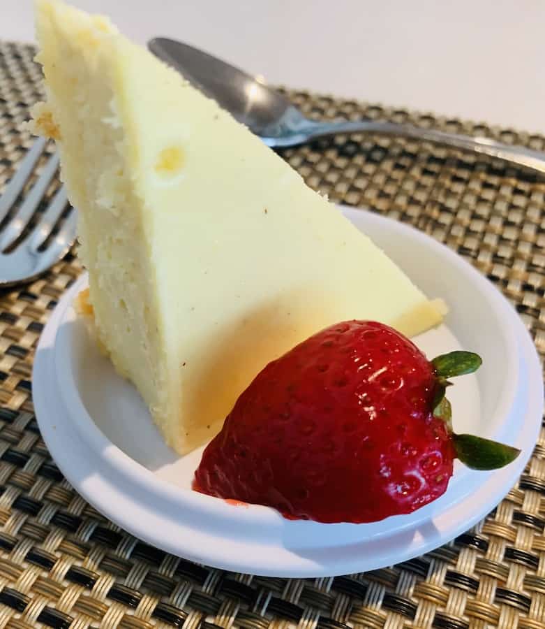 a triangle of cheesecake standing up on a small plate next to a strawberry