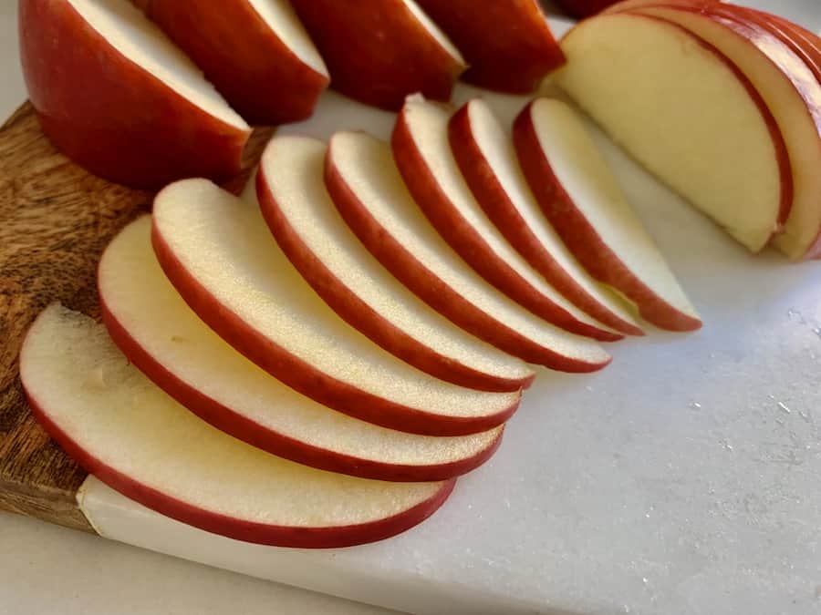 thinly sliced apples fanned out on a cutting board, with larger slices in the background