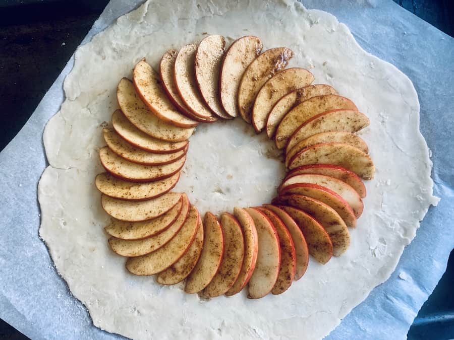 rolled out pie dough on parchment paper topped with aa circle of layered apple slices