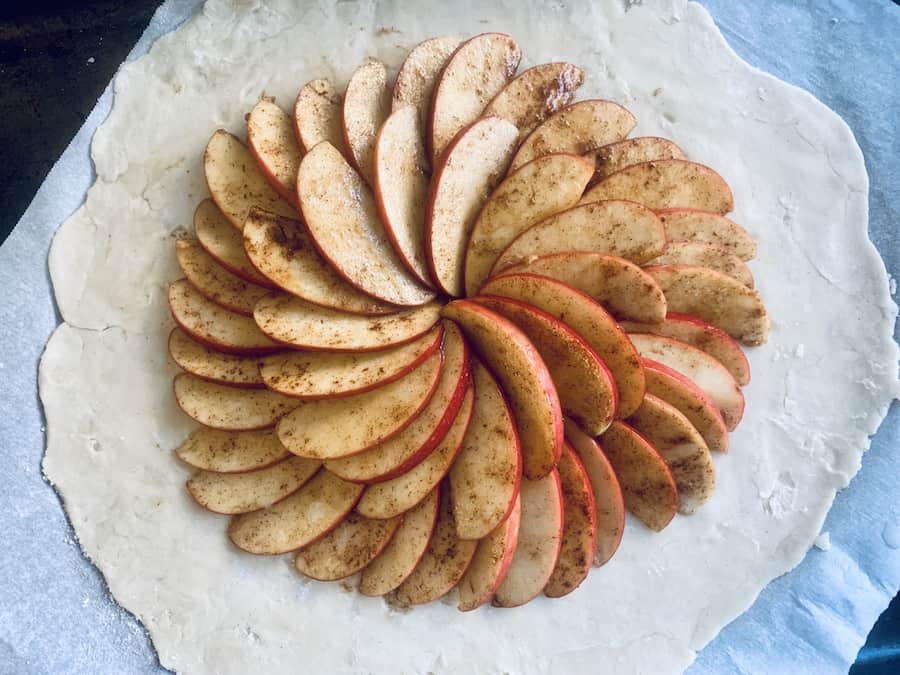 rolled out pie dough on parchment paper topped with two circles of layered apple slices, they have the appearance of a flower blossom