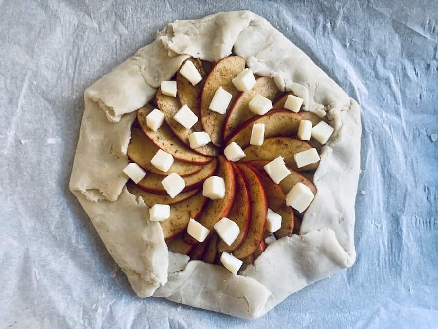 top view of raw apple galette with the dough folded over the apple filling and dots of butter scattered over the filling