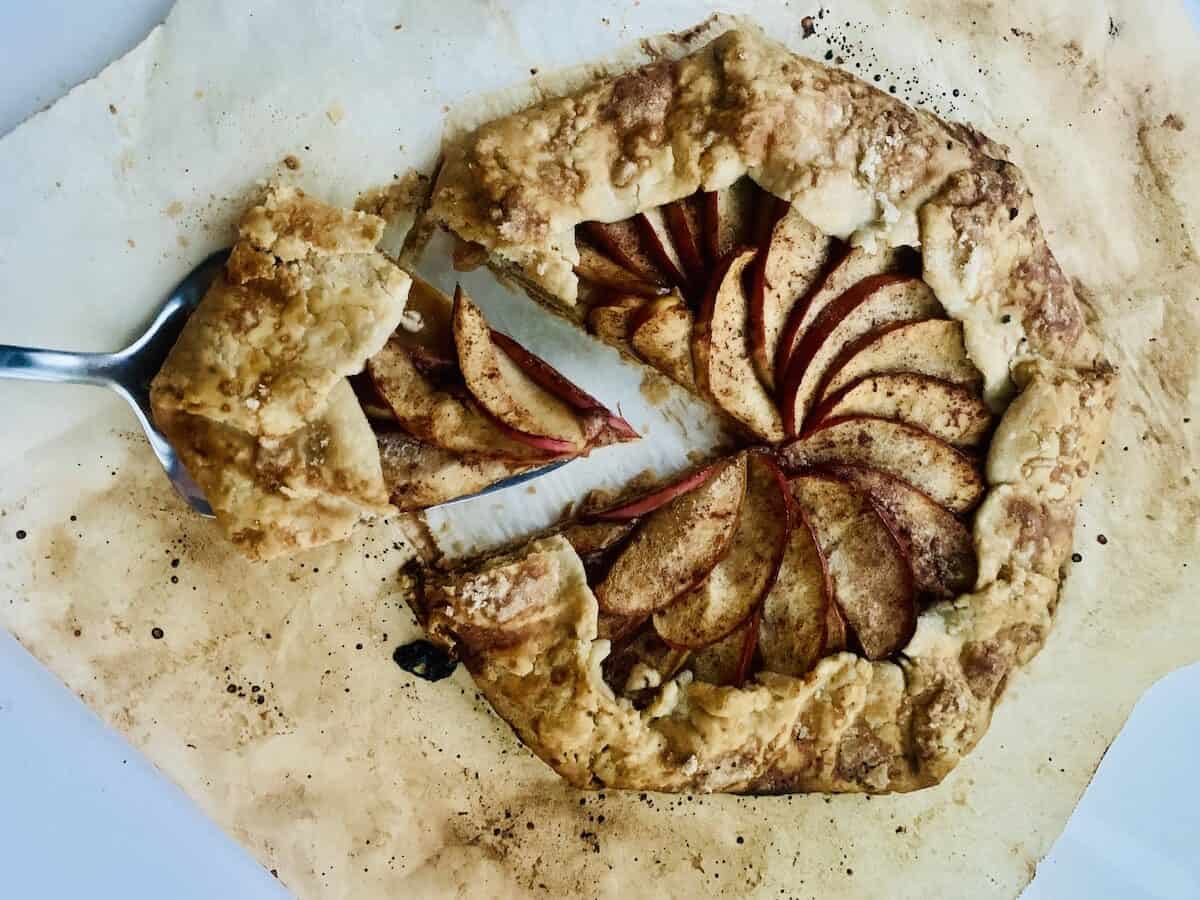 gluten-free apple galette on browned parchment paper, with a cake lifter holding out one slice