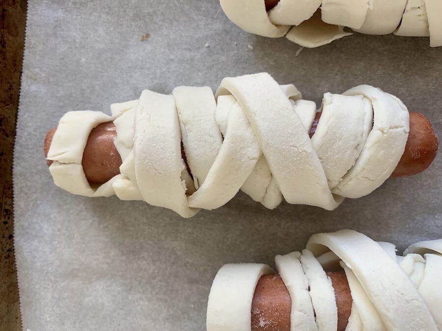 gluten-free mummy hot dogs wrapped in raw gluten-free puff pastry, on a baking sheet with parchment paper