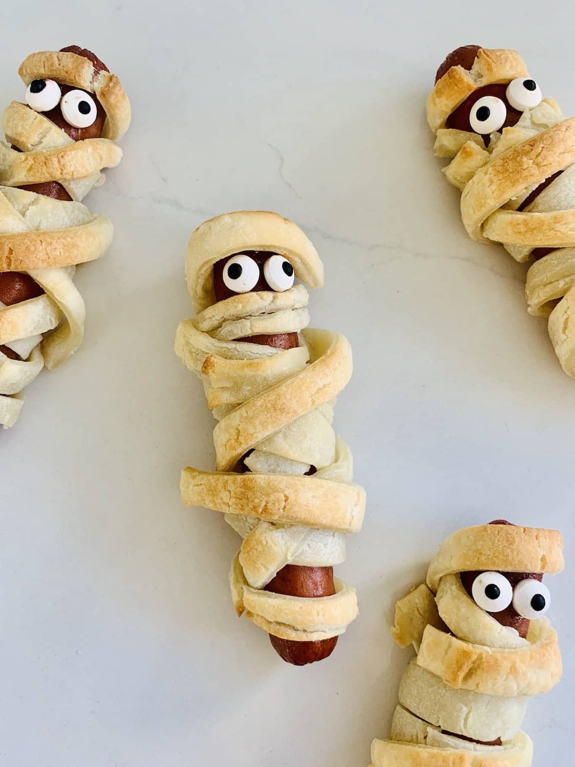 A gluten-free mummy hot dog wrapped in gluten-free puff pastry with candy eyes.