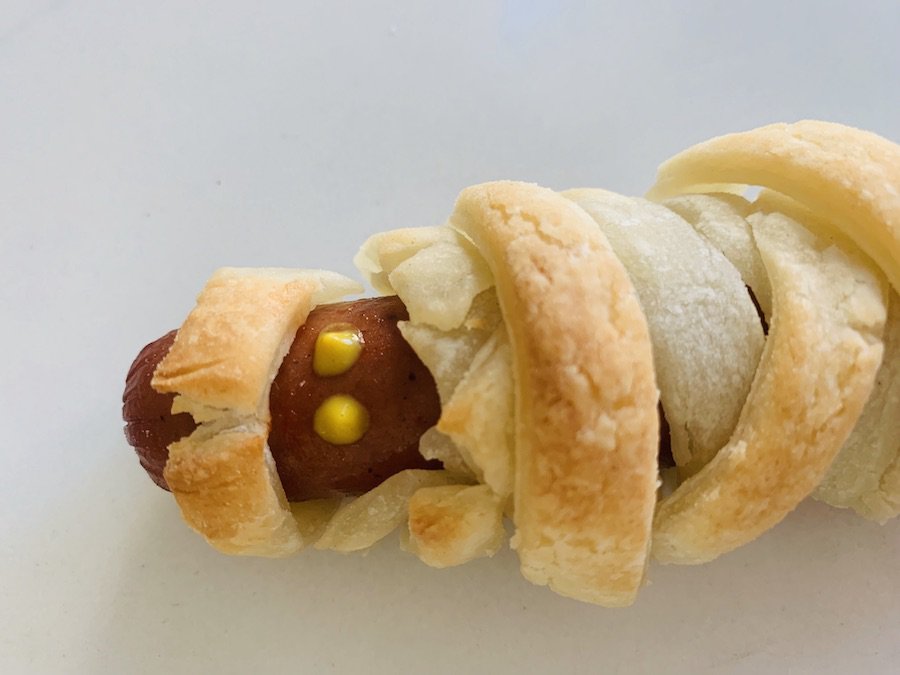 a gluten-free mummy hot dog wrapped in gluten-free puff pastry with dots of yellow mustard for eyes