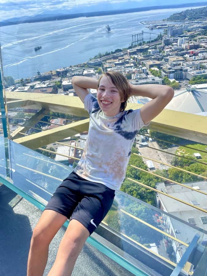 CJ sitting on a glass bench and leaning on a glass wall at the top of the Space Needle
