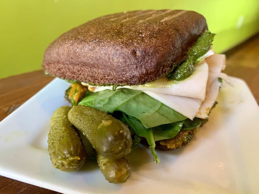 gluten-free turkey sandwich with pesto sauce, side of three cornichon pickles