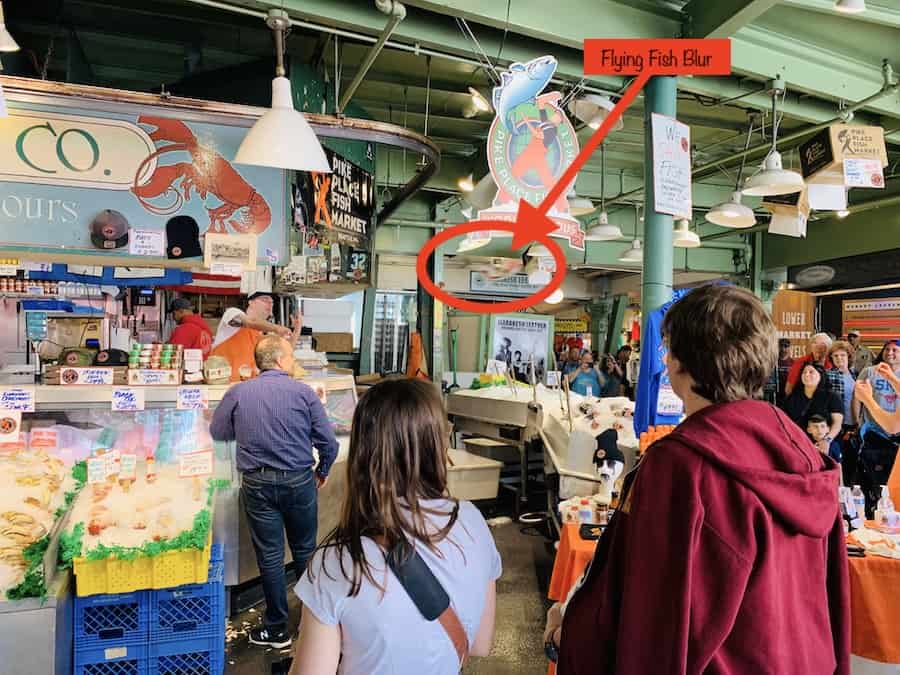 fish stand at Pike Place Market, employees throwing fish, with a blurred object circled in red and identified as "flying fish