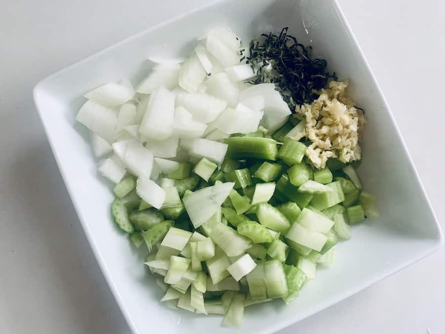 bird's eye view of chopped celery, onions and rosemary and diced onions in a square white bowl