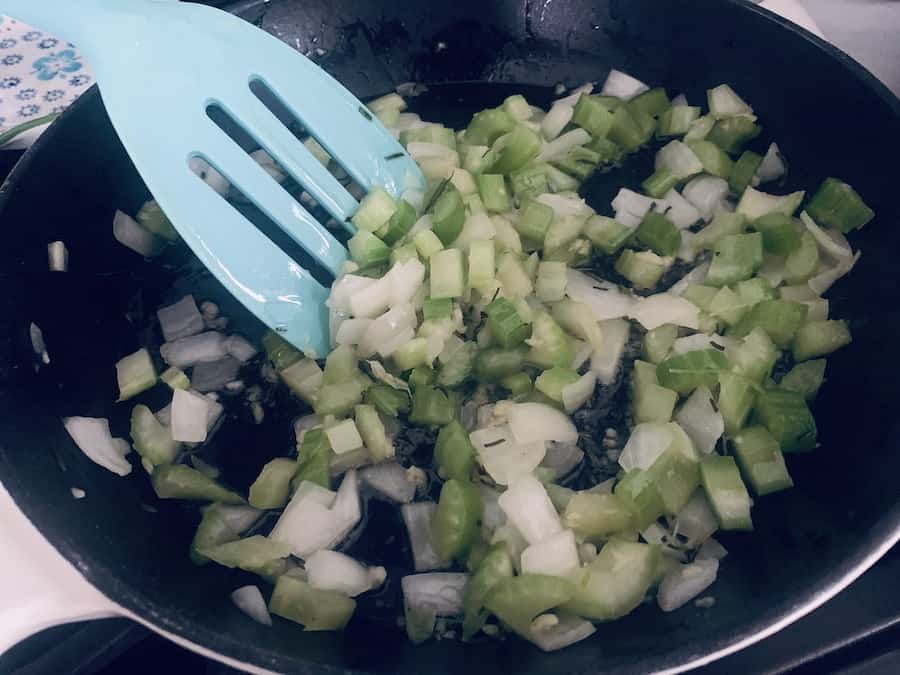translucent onions, celery, and spices being moved by an aqua slotted spatula in a skillet