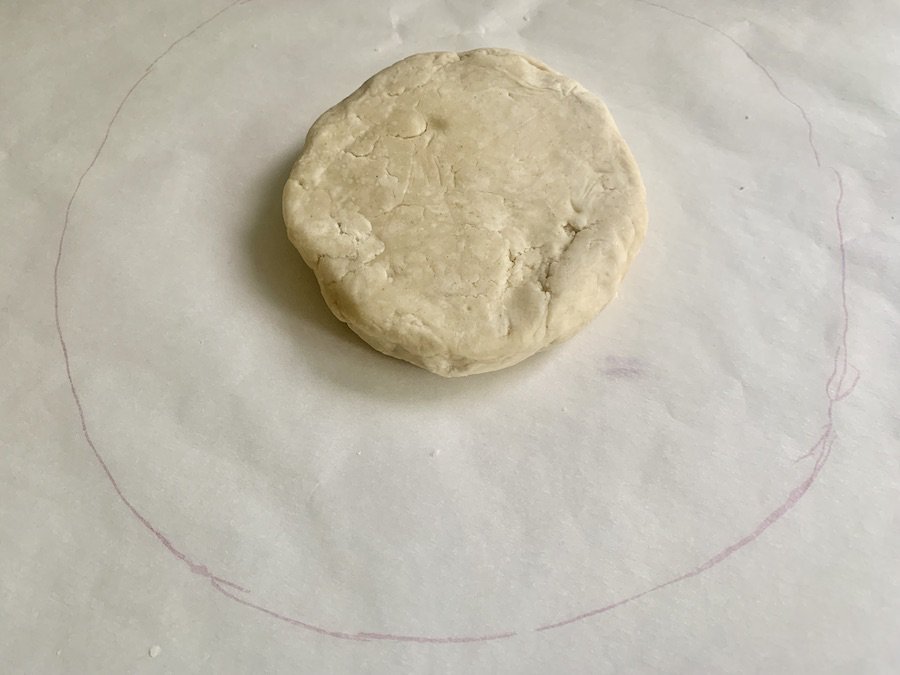 a round disk of pie dough on parchment paper with a pink circle drawn on it