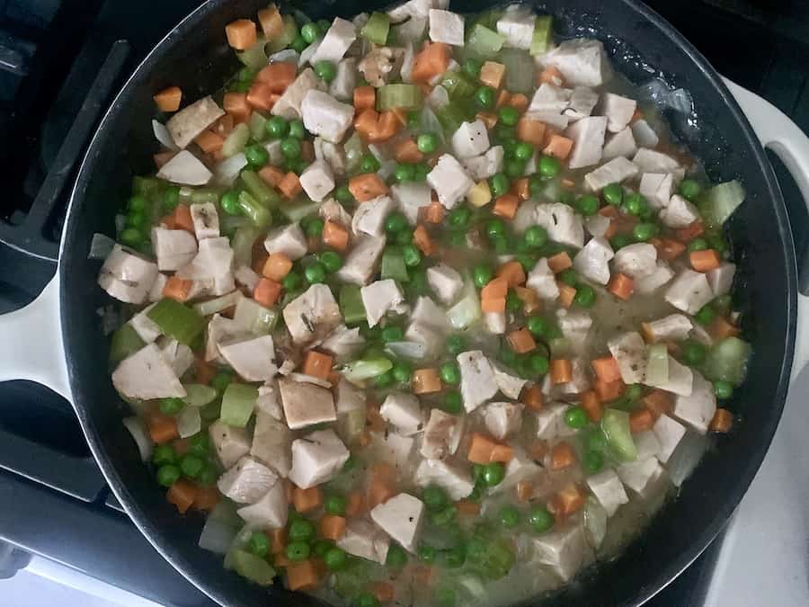 bird's eye view of a skillet with pot pie filling, turkey, peas, and carrots are most visible