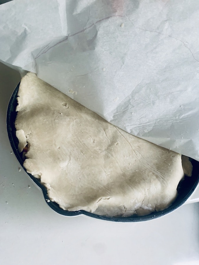 parchment paper being pulled back from a skillet covered with gluten-free pie dough, bird's eye view