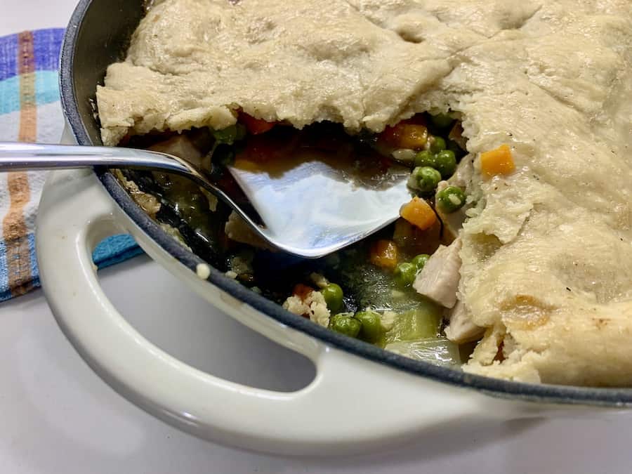 partial view of skillet with turkey pot pie... slice of crust removed and a cake lifter left behind, blue and orange gingham dish towel in the background