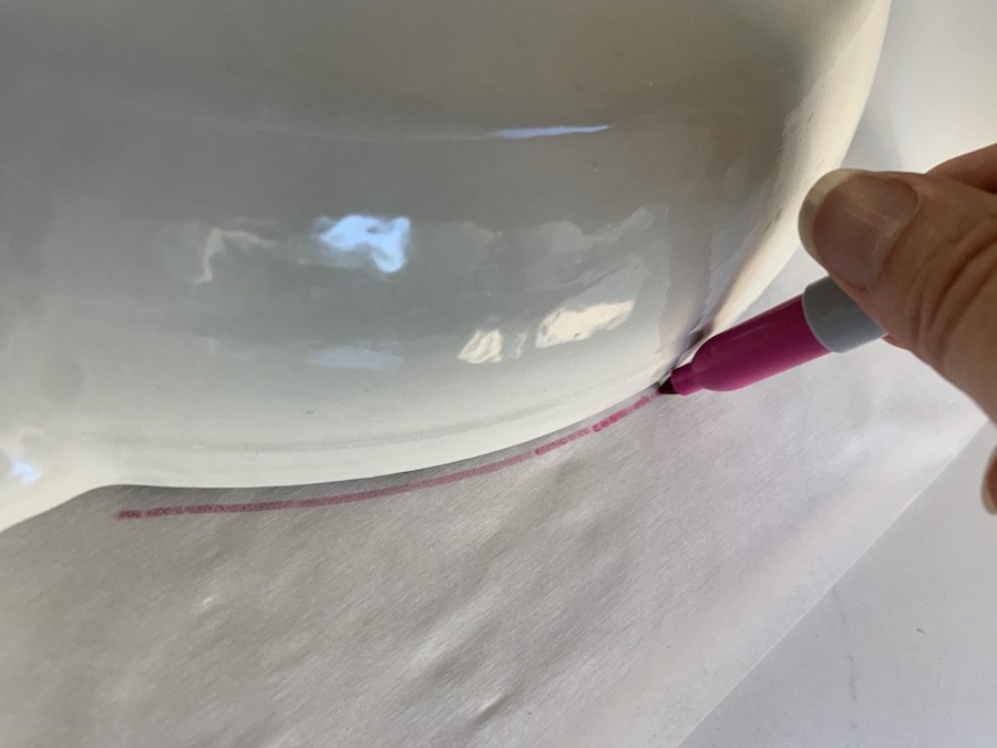 tracing edge of cream enameled skillet onto parchment paper with pink sharpie