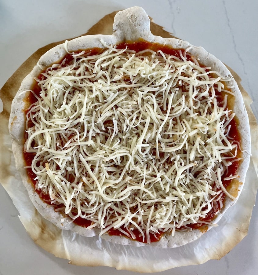 Pumpkin shaped pizza topped with red sauce and shredded mozzarella cheese before melting.