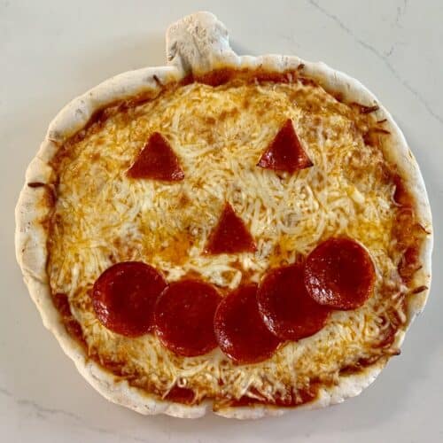 Gluten-free jack-o-lantern pizza,topped with sauce, cheese, and pepperoni triangle eyes and nose and 5 circles shaped into a smile.
