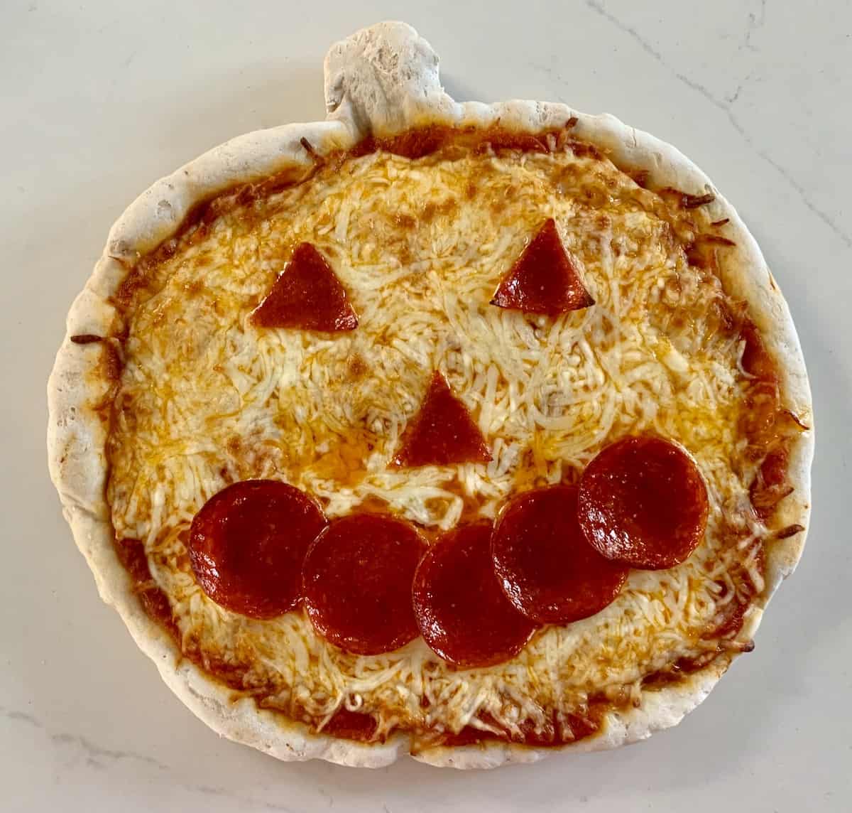 Gluten-free jack-o-lantern pizza,topped with sauce, cheese, and pepperoni triangle eyes and nose and 5 circles shaped into a smile.