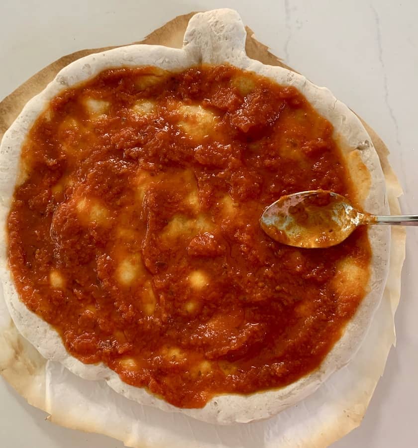Spoon covered with tomato sauce resting on pumpkin shaped pizza topped with red sauce.