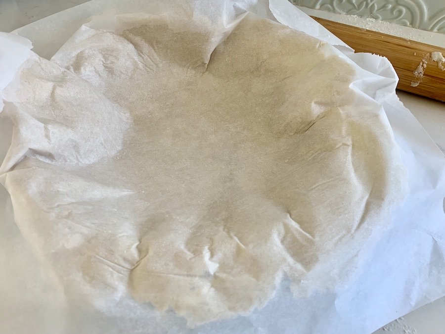 pie dough sitting mostly on top of a pie pan with parchment paper still on top