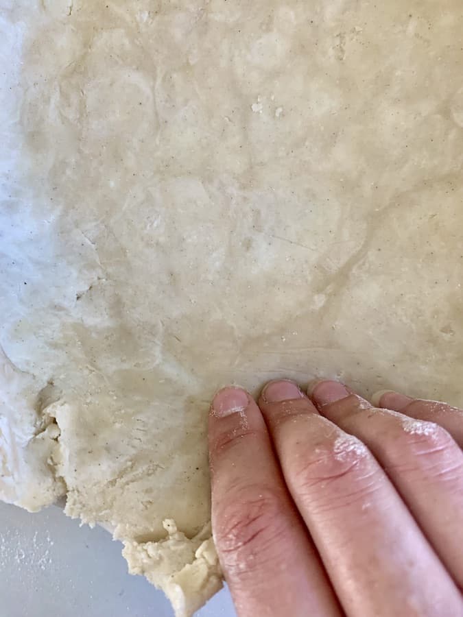 fingers pushing pie dough into the corners of a pie pan