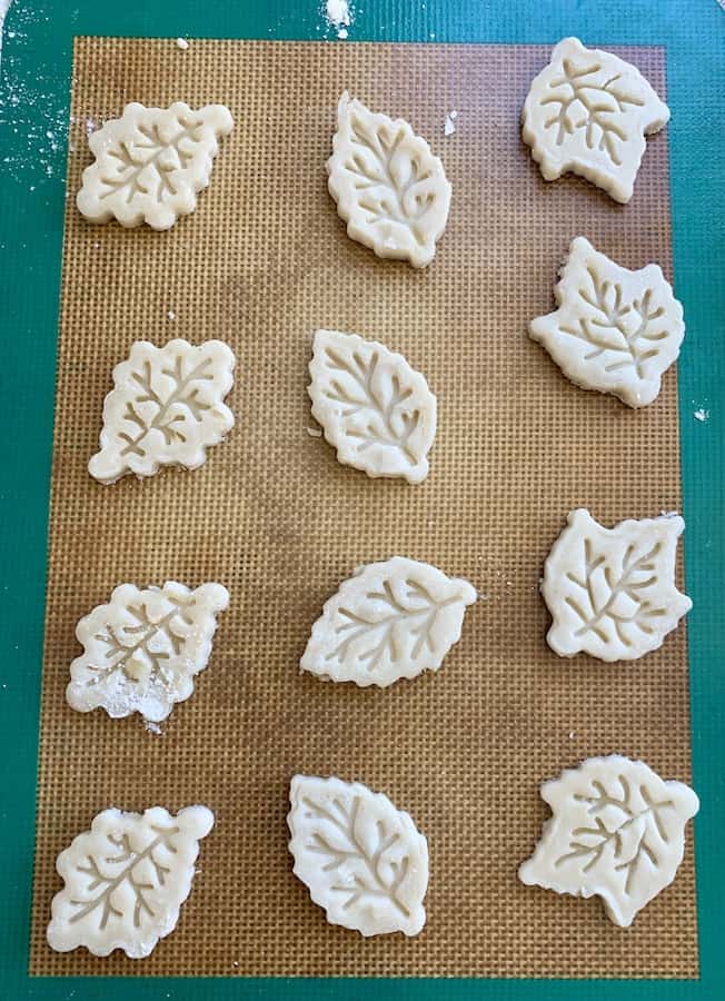 birds eye view: unbaked leaf pastry cut-outs on a silicone baking mat with green trim