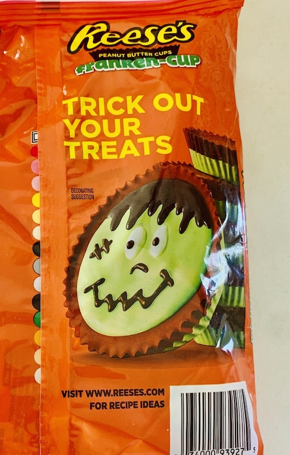 Orange package with a Reese's Peanut Butter Cup decorated with green and brown frosting to look like Frankenstein. Text "Trick out your treats" and "visit www.reeses.com for recipe ideas"