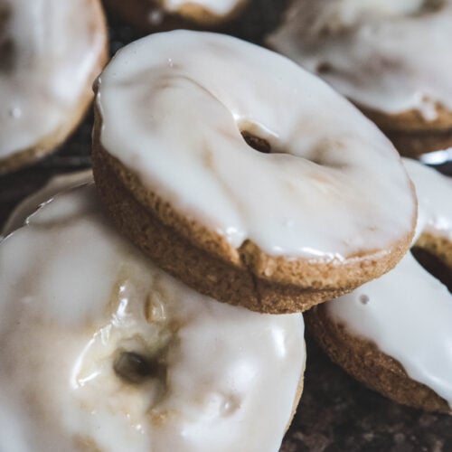 A pile of baked gluten-free maple donuts topped with white icing.