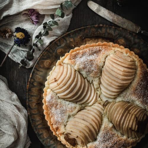 Birds' eye view of of a pear tart with four pear halves sliced and placed in the tart branching out from the center as if they were flower petals.
