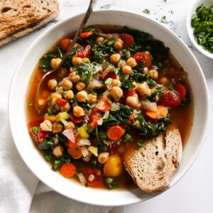 Birds eye view: bowl of sop with veggies, chickpeas and a slice of bread in the soup.