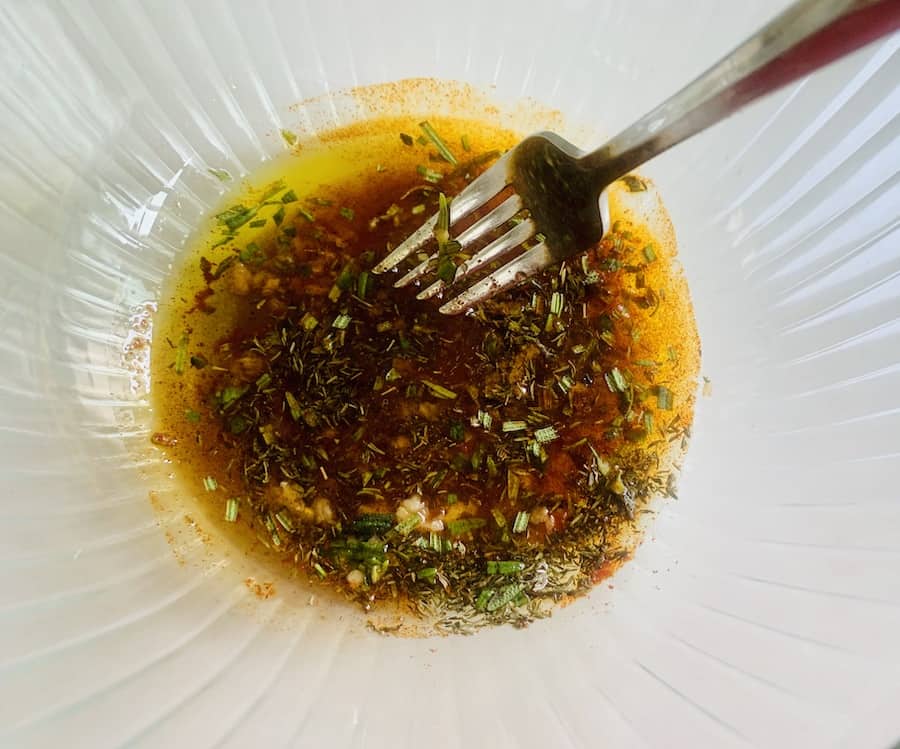 Fork resting in a glass bowl of a brownish-orange marinade with spices.