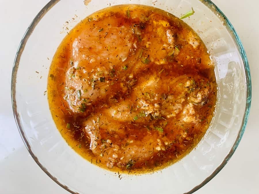 Bird's eye view of a glass bowl containing two raw turkey tenderloins immersed in a brownish-orange marinade.
