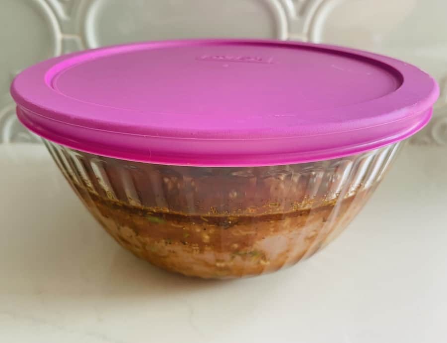 Pyrex bowl with a purple lid. Bowl contains marinade and raw chicken.