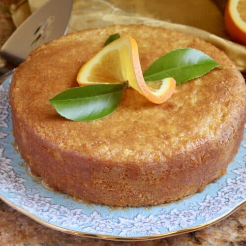 A round orange cake, topped with a slice of orange (twisted) and two green leaves.