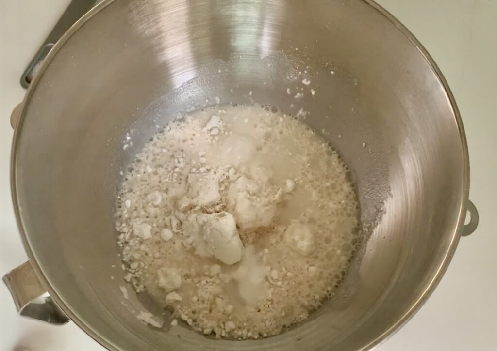 White, dry ingredients in a metal mixing bowl with liquid with little bubbles.