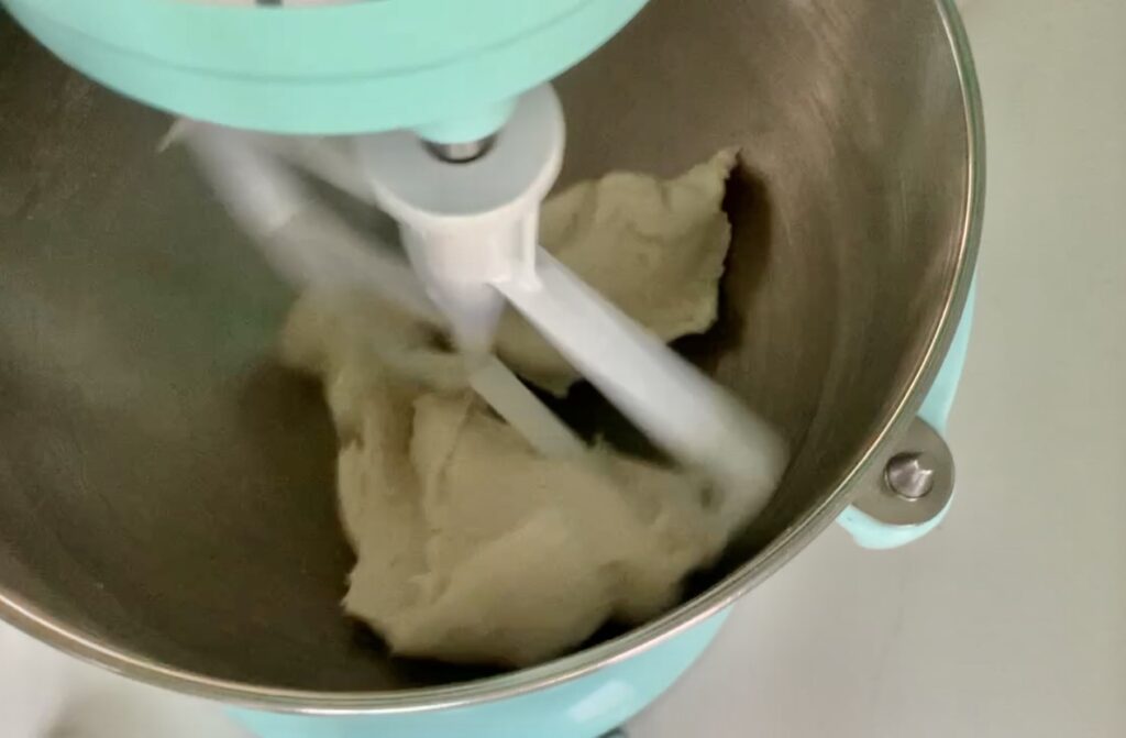 Top view of part of aqua stand mixer and metal bowl with dough being mixed.