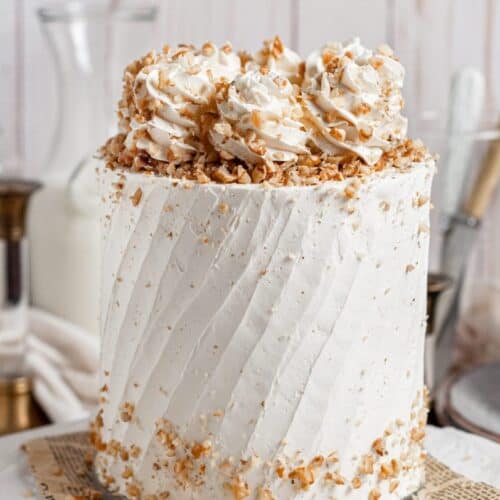 tall white cake topped with whipped cream and walnut pieces, walnut pieces also scattered along the bottom 1-2" of the cake.